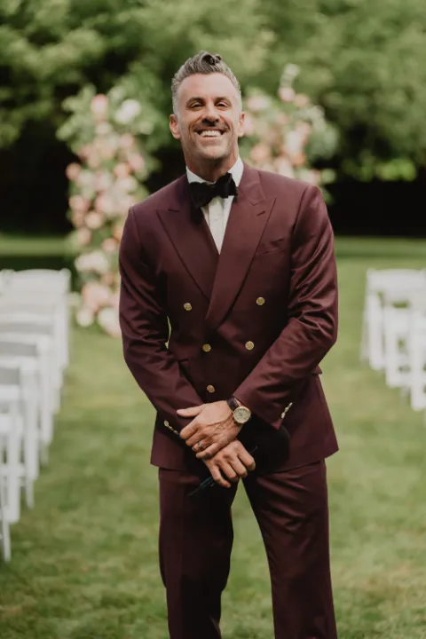 Jeff wearing a burgundy double-breasted suit, smiling, holding a microphone, and looking at the camera.